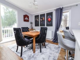 A dining area with a wooden table surrounded by black chairs on a gray rug beside a window with dark curtains at 155 Woodland Hall Lyons in Ruthin