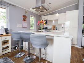 A kitchen with an island counter and three grey bar stools a vase with flowers on the counter white cabinets and wooden floor at 155 Woodland Hall Lyons in Ruthin