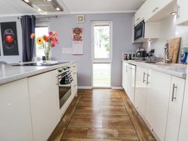 A kitchen with white cabinets and wooden floor with flowers on an island at 155 Woodland Hall Lyons in Ruthin
