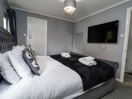 A bedroom with a bed with white linens and black throw blanket a wall-mounted television and a door at 155 Woodland Hall Lyons in Ruthin