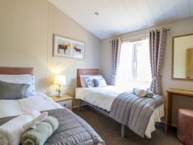 A bedroom with two single beds bedside table lamp window with curtains and a mirror at The Owlet in Dolwen near Llanidloes