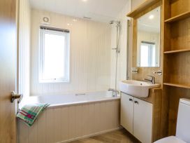 A bathroom with a bathtub shower sink mirror shelves and a towel at The Owlet in Dolwen near Llanidloes
