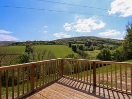 A wooden deck with railing overlooking green fields and hills at The Owlet in Dolwen near Llanidloes