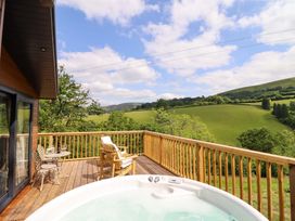 A deck with a hot tub and seating overlooking a landscape at The Owlet in Dolwen near Llanidloes
