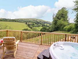 A deck with a hot tub and chair overlooking hills at The Owlet in Dolwen near Llanidloes