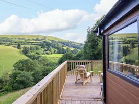 A wooden deck area with a chair overlooking hills at The Owlet in Dolwen near Llanidloes
