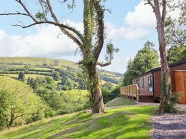 A cabin with a deck beside a tree and hill at The Owlet in Dolwen near Llanidloes