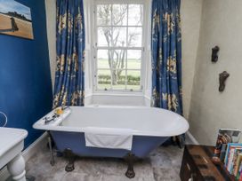 A bathroom with a bathtub and curtains at Elford Farmhouse in Seahouses