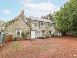 A house with a gravel parking area and trees at Elford Farmhouse Seahouses