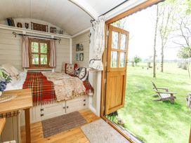 A small room with a built-in bed covered with blankets and pillows next to an open wooden door leading to a grassy yard with a wooden chair at Sika in Warmwell