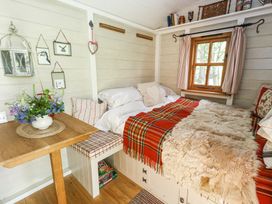 A small room with a bed covered with a red plaid blanket and sheepskin next to a wooden table with flowers at Sika in Warmwell
