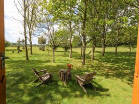 A garden view with two wooden chairs and a tree stump table with flowers among trees at Sika in Warmwell