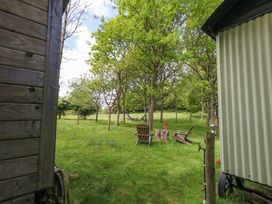 A grassy outdoor area with trees a hammock between trees wooden chairs and a table with flowers at Sika in Warmwell