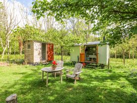 Two small wooden cabins in a grassy area with trees and outdoor wooden table and chairs with red flowers at Fallow in Warmwell