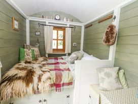 A small room with a bed covered by throws and pillows near a window with curtains and green wooden walls at Fallow in Warmwell