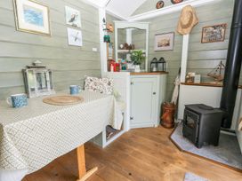 A small dining area with a table and two mugs a wood stove and a cabinet with decorations at Fallow in Warmwell