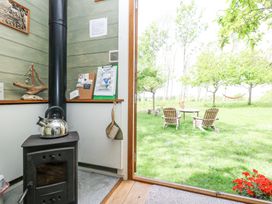 A wood stove inside a wooden cabin with a view of a garden with chairs and trees at Fallow in Warmwell
