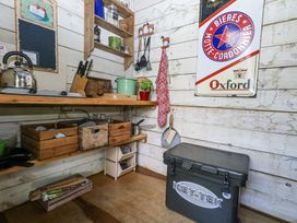 A small kitchen area with wooden shelves holding utensils and containers and a cooler box on the floor at Fallow in Warmwell