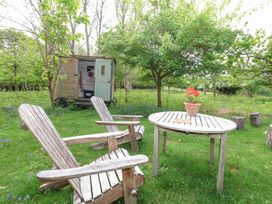 A garden with two wooden chairs and a round table with a potted plant and a book near a small wooden shed with an open door at Fallow in Warmwell