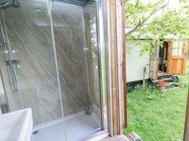 A shower area with glass doors and a sink next to an open wooden door leading to a grassy outdoor area with a small structure on wheels at Fallow in Warmwell