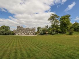 A large stone manor house with multiple chimneys surrounded by a lawn and trees at Fallow in Warmwell