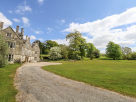 A large stone house with chimneys next to a curved gravel driveway and green lawn with trees at Fallow in Warmwell