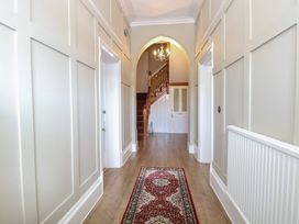 A hallway with light-colored paneled walls wooden flooring a patterned rug two doors and a staircase with a chandelier at The Burleigh in Hunstanton