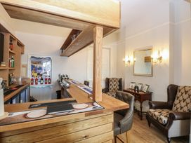A small bar area with wooden counters stools and armchairs near a side table with framed pictures at The Burleigh in Hunstanton