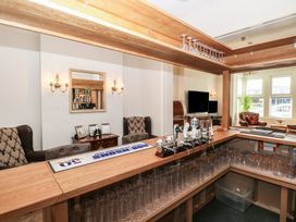 A home bar setup with taps glasses and seating area with armchairs and TV at The Burleigh in Hunstanton