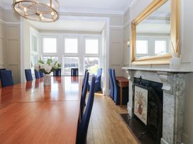 A dining room with a long wooden table and blue chairs by large windows and a marble fireplace with a mirror above at The Burleigh in Hunstanton