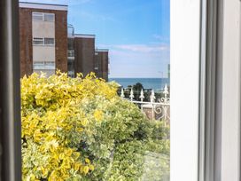 View through a window showing yellow and green bushes a railing a brick building and the sea in the background at The Burleigh in Hunstanton