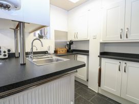 A kitchen with white cabinets black countertops a stainless steel sink and various appliances at The Burleigh in Hunstanton