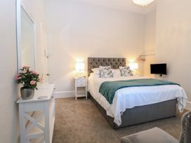 A bedroom with a double bed bedside tables lamps a dresser with flowers and a mirror at The Burleigh in Hunstanton