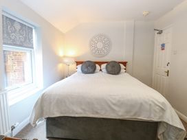 A bedroom with a large bed with white bedding and two round gray pillows a window with patterned blinds a table lamp and a decorative wall hanging above the bed at The Burleigh in Hunstanton