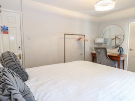 A bedroom with a bed white bedding and grey pillows a wooden desk with a grey chair and a round mirror on the wall at The Burleigh in Hunstanton
