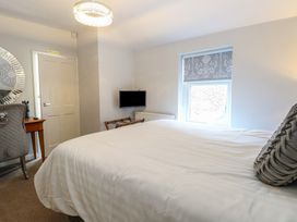 A bedroom with a bed a window a wall mounted tv a chair a wooden desk and a decorative round mirror at The Burleigh in Hunstanton