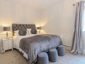 A bedroom with a double bed bedside tables with lamps stools at the foot of the bed and curtains at The Burleigh in Hunstanton