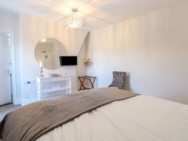 A bedroom with a bed a wall-mounted TV a round mirror a chair and a small white cabinet at The Burleigh in Hunstanton