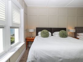 A bedroom with a large bed two green round cushions two bedside tables with lamps and windows with shutters at The Burleigh in Hunstanton