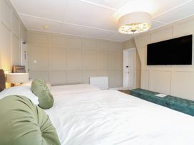 A bedroom with two beds green round pillows a wall-mounted television and a long green bench at The Burleigh in Hunstanton