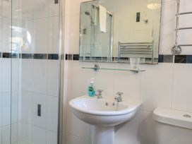 A bathroom with a shower enclosure a pedestal sink with two taps a wall mirror a glass shelf with a cup and soap dispenser and a toilet at The Burleigh in Hunstanton