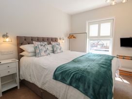 A bedroom with a bed with white sheets and a green throw blanket a nightstand with lamps and a window with shutters at The Burleigh in Hunstanton