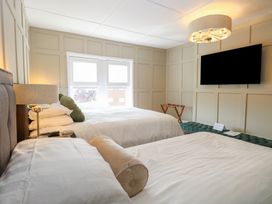 A bedroom with two beds a wall-mounted TV a window and a bedside lamp at The Burleigh in Hunstanton