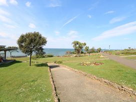 A paved pathway through a grassy park with trees and flower beds by the sea at The Burleigh in Hunstanton