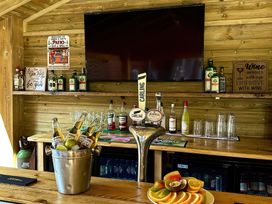 A wooden bar with bottles, glasses, a fruit plate, a bucket with beers, signs, and a large TV mounted on the wall at The Burleigh in Hunstanton