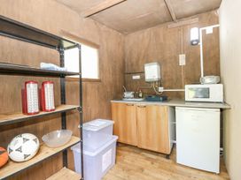 A small kitchen area with wooden cabinets a mini fridge microwave sink shelving unit with soccer balls and plastic storage containers at Moonlight in Ventnor