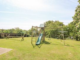 A grassy backyard with a wooden playset including a slide and swings surrounded by trees at Moonlight in Ventnor