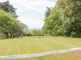 A grassy field with a wire fence and trees surrounding it and a view of the sea at Moonlight in Ventnor