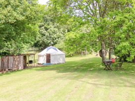 A grassy garden with a yurt, wooden shelter, chairs, table, and trees at Stardust in Ventnor