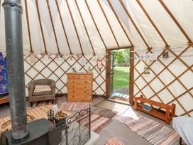 Interior of a yurt with a wood stove armchair wooden dresser rugs on the floor and a door open to grass outside at Stardust in Ventnor